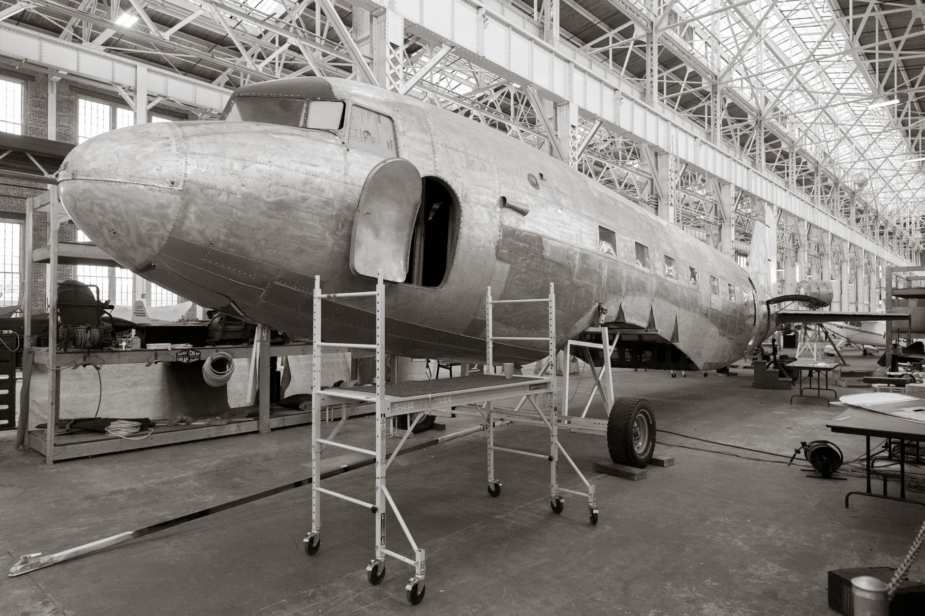 A classic aircraft undergoes restoration inside a spacious hangar, showcasing industrial architecture.