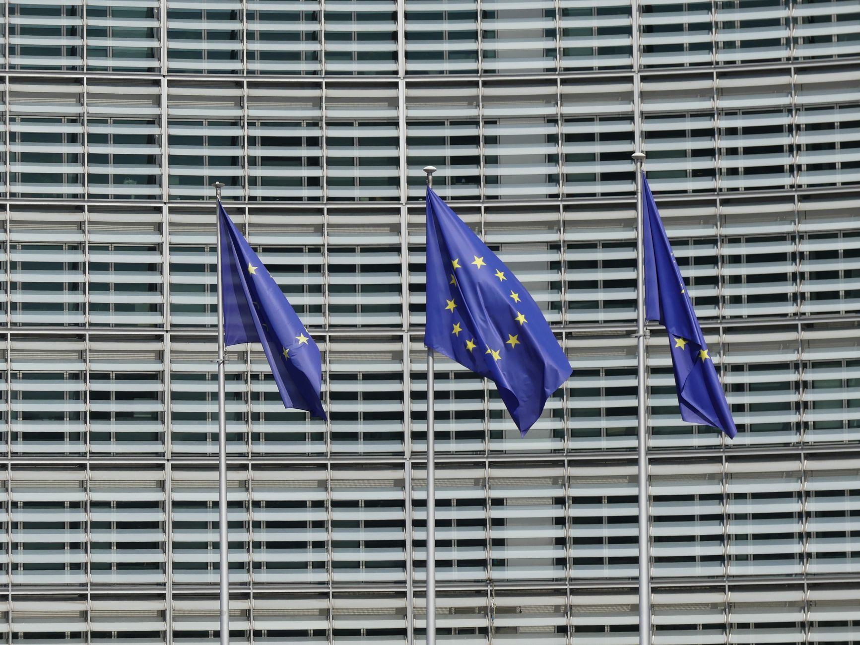 Three European Union flags waving outside the Berlaymont building in Brussels, Belgium.