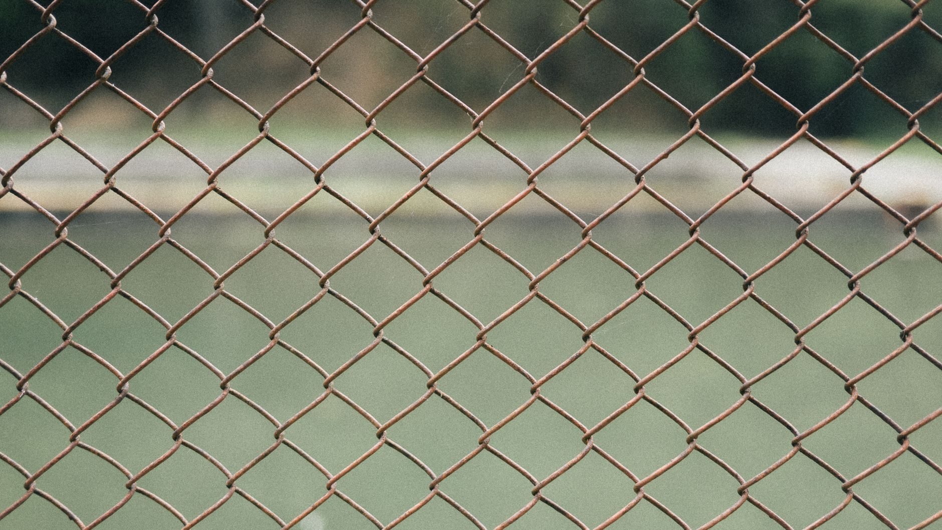 Close-up view of a rusty chain-link fence with blurred background, outdoors.