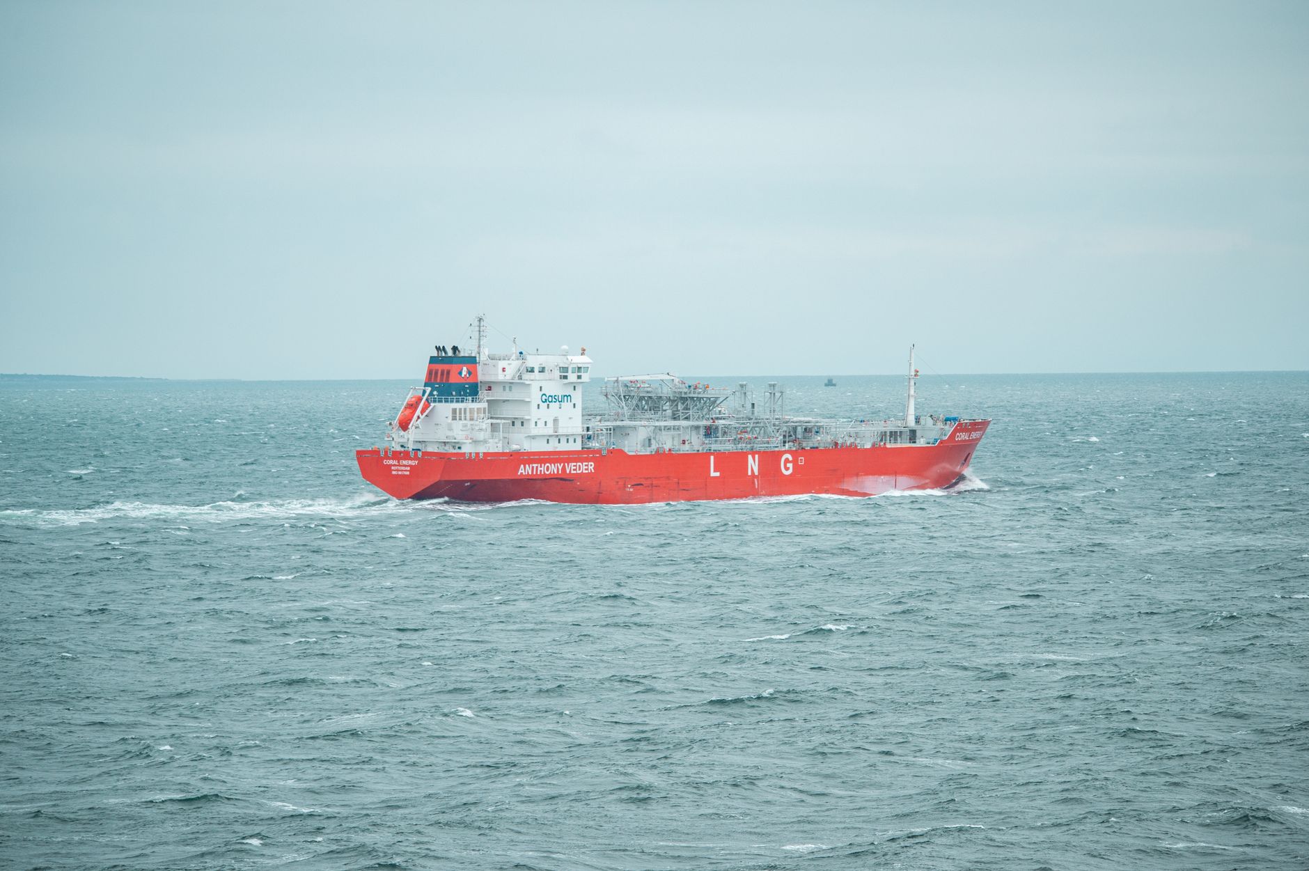 A red LNG carrier sailing on calm seas under a cloudy sky, showcasing marine transportation.
