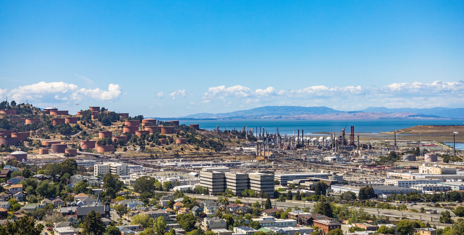 Aerial view of an urban area with an oil refinery by the sea and mountains.