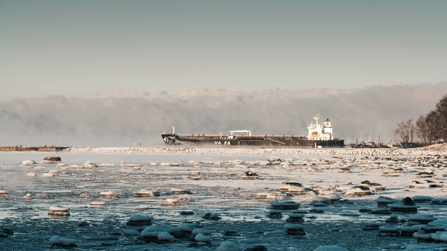Cargo ship navigating through icy waters in a winter landscape.