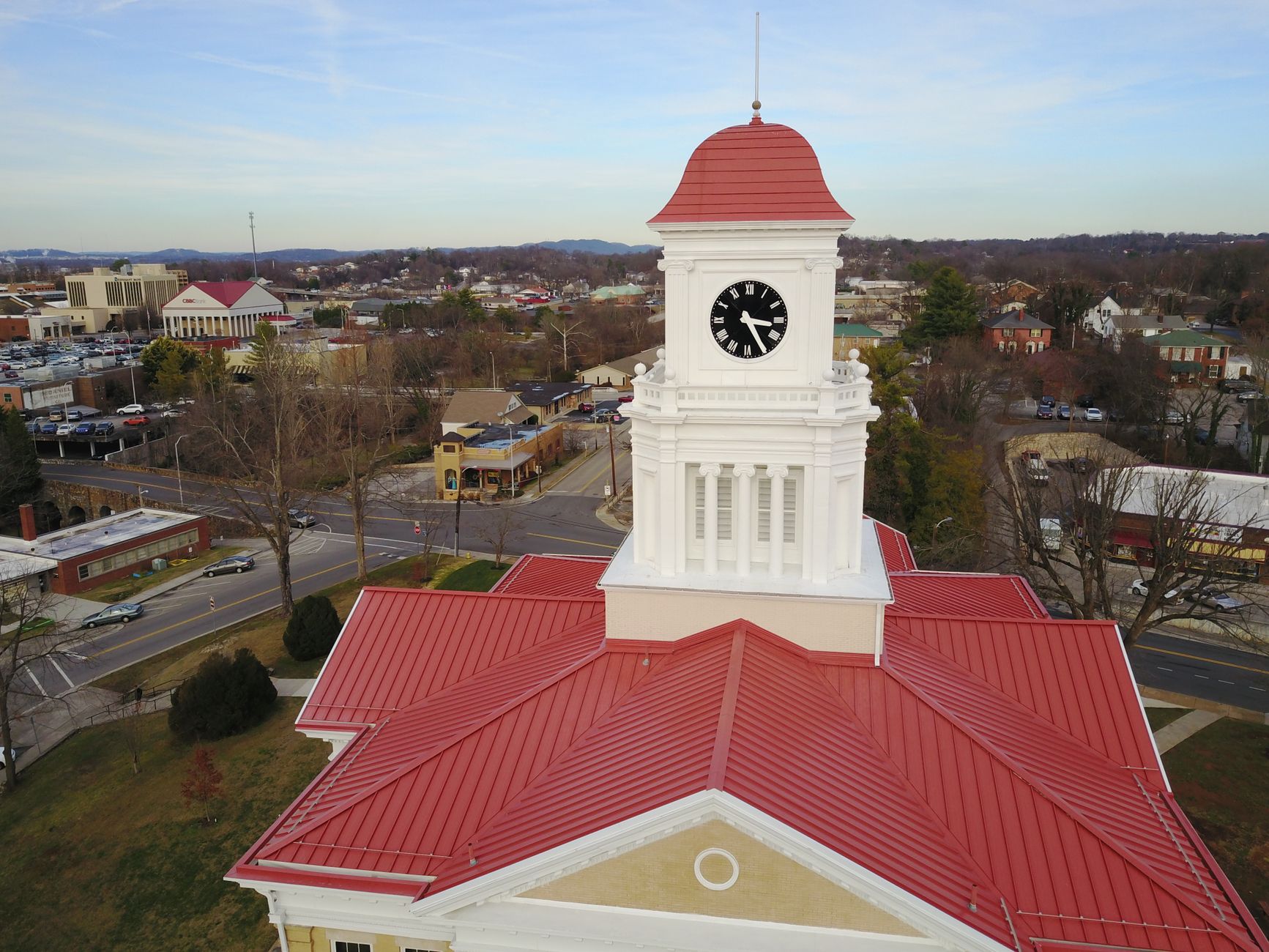 Aerial shot of a historic courthouse with clock tower featuring red roof and cityscape background.