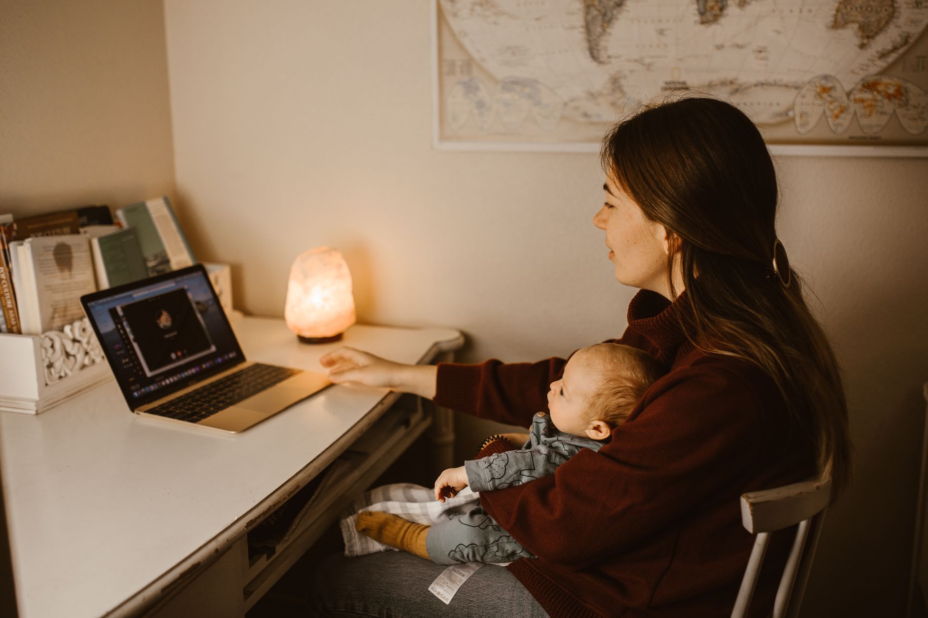Mother holding her newborn at a desk while reading on a laptop