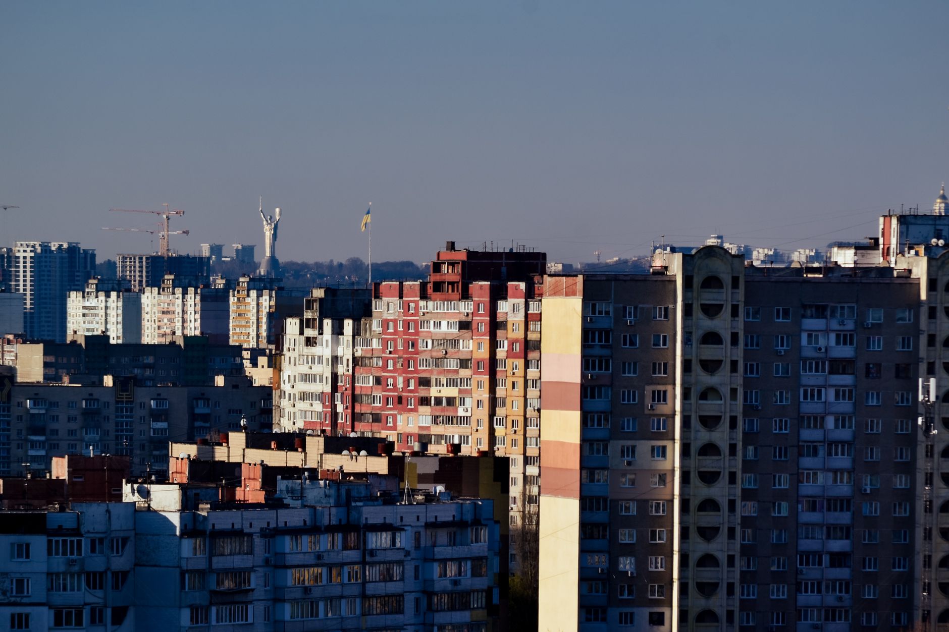 Aerial view of Kyiv's skyline featuring Soviet-era apartment blocks and the Motherland Monument.