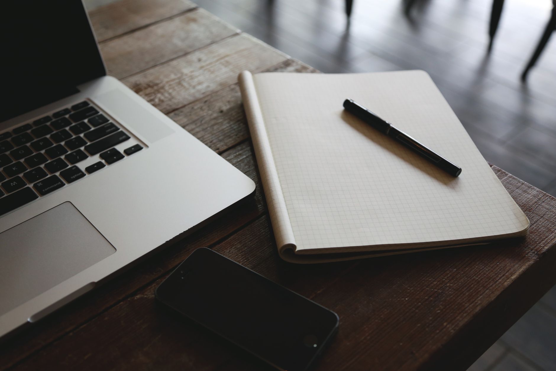 A minimalist desk setup featuring a laptop, smartphone, and notepad with pen, ideal for productivity.
